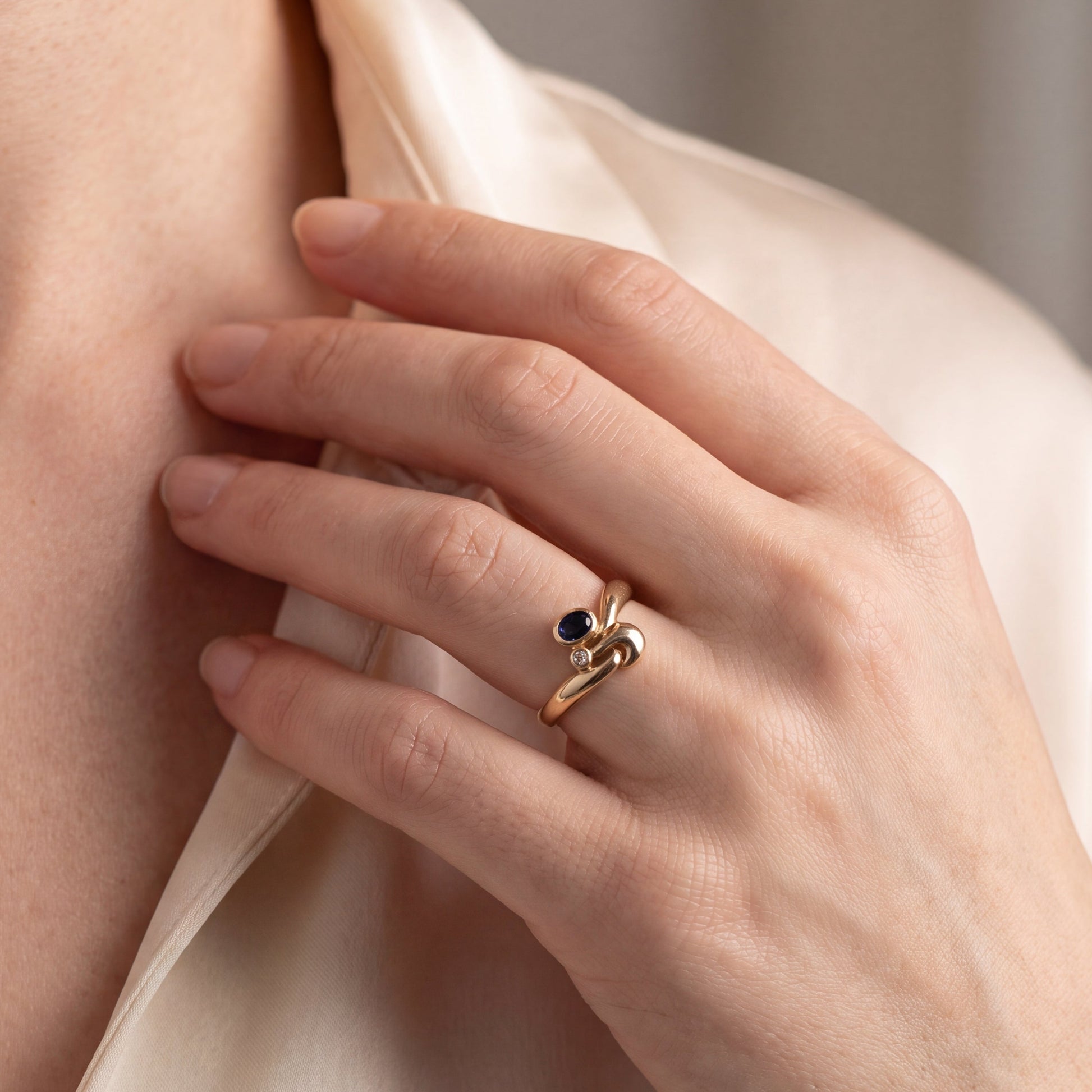 yellow gold ring with sapphire and diamond on finger 
